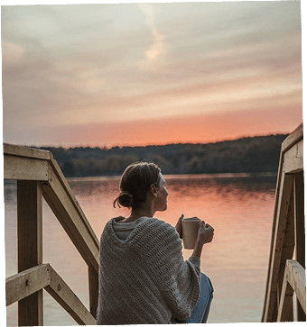 Mid-age woman sitting in front of a lake, calmly admiring the sunset and meditating